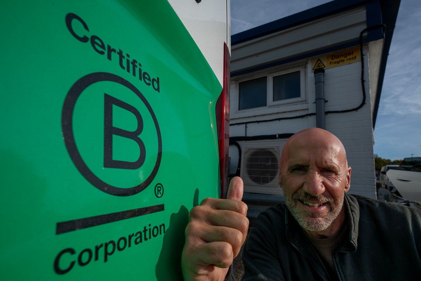 Adam from the Source team giving a thumbs up beside the Certified B Corporation mark on a Source van