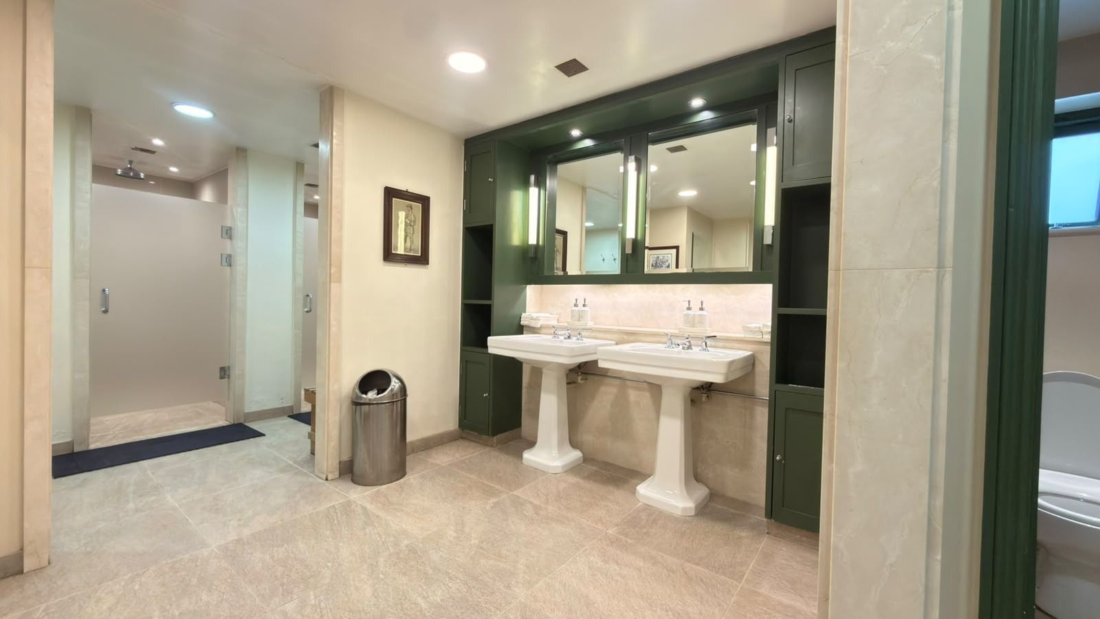 A golf club changing room: two pedestal basins under green cabinets and mirrors, with the showers beyond