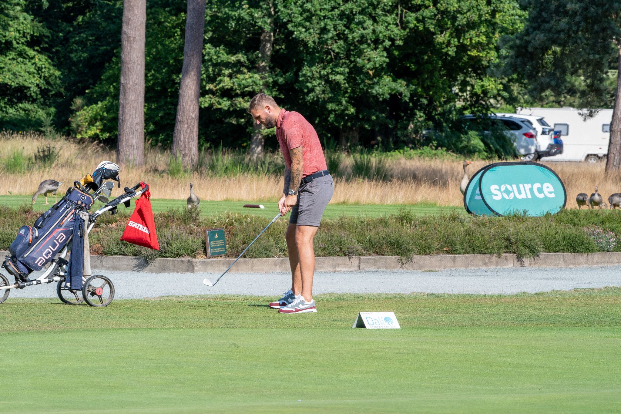 A golfer driving off a tee beside a Source banner at a golf day
